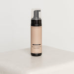 Self-tanning mousse bottle on a white surface with a white background