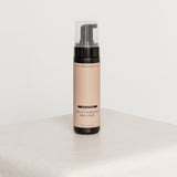Self-tanning mousse bottle on a white surface with a white background