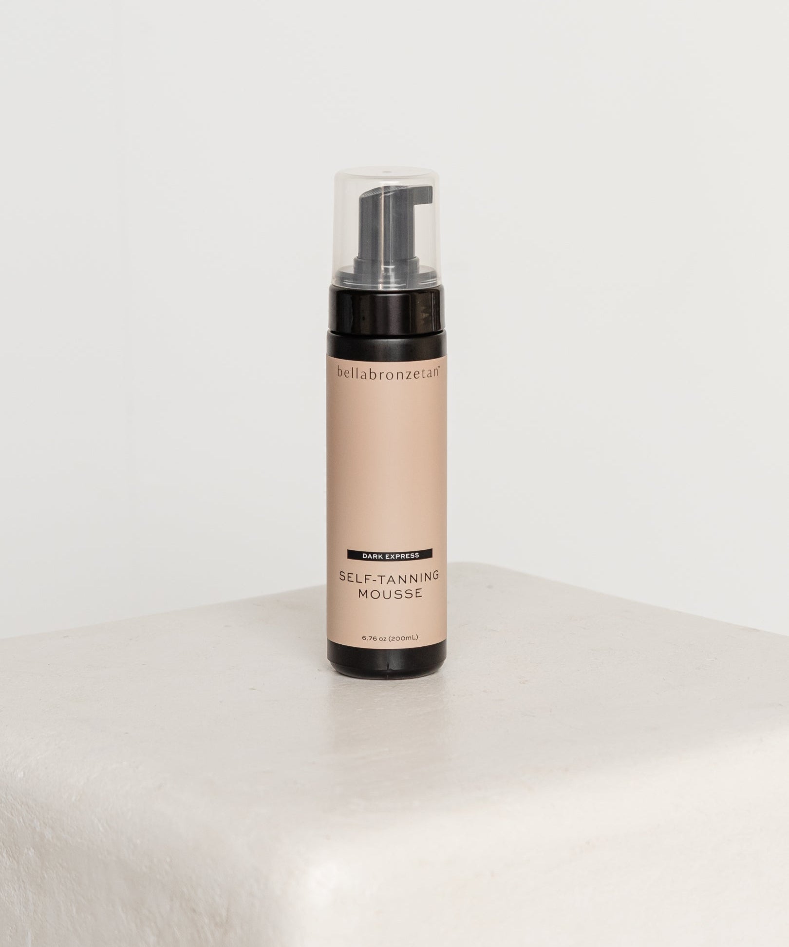 Self-tanning mousse bottle on a white surface with a white background