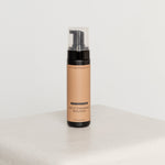 Self-tanning mousse bottle on a white surface with a light gray background